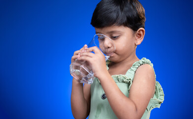 Side view of Girl kid busy drinking water on blue background - concept of healthy purified drinking...