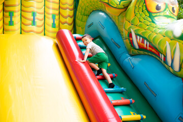 Little boy child climbs the stairs of a multi-colored slide in the park.