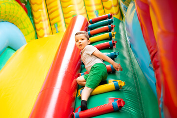 Fototapeta na wymiar Little boy child climbs the stairs of a multi-colored slide in the park.