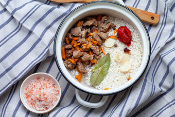 Raw materials for cooking pilaf, rice and lamb meat, grated carrots and chopped onions, peppers, tomatoes, garlic, herbs and spices. Gray background, top view copy space