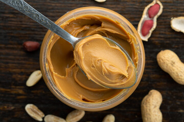 Peanut butter in an open jar and heap of nuts on wood background.