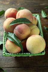 Ripe peaches in a basket on a wooden table with scattered leaves.