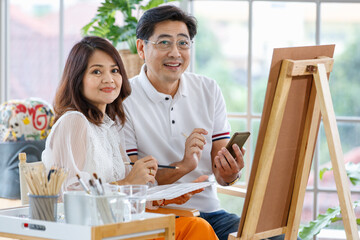 Senior man and woman couple, husband and wife, painting image together in home gallery with warm and happy circumstance. Idea for time-sharing and relaxing for older people after retirement