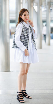 Vertical Front View Full-length Body Portrait Of Cute Smiling Young Adult Asian Woman With Brown Hair, Trendy Modern Clothes And High Heels Shoes, Walking Toward On The Street And Looking To Camera