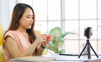 portrait of young beautiful asian woman sitting on a floor smiling while showing how to make origami paper via smartphone. Work and study from home concept