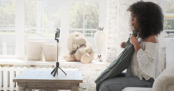 Young afro blogger streaming online in a social network for followers, showing stylish dress, recording video blog on smartphone about brands and trends of the season, fashionable style of clothing