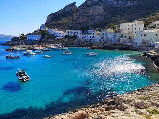 View on the Spiaggia di Cala Dogana bay with boats surrounded by white houses and hills in Levanzo - Aegadian Islands, Sicily, Italy