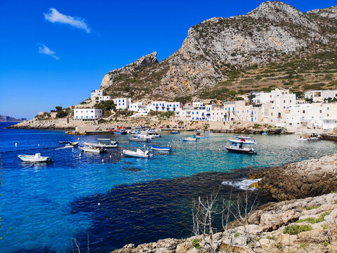 View on the Spiaggia di Cala Dogana bay with boats surrounded by white houses and hills in Levanzo - Aegadian Islands, Sicily, Italy