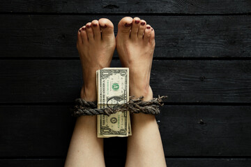 tying a leg with an old rope of a young girl and American dollars on nohs on the black floor, human trafficking, slavery ransom
