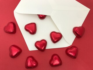 ハート型のチョコレートと白い封筒（赤背景・下向きにあふれるチョコ）、バレンタイン・ホワイトデーイメージ