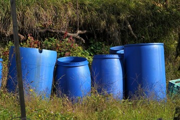 Plastic barrels for fermentation of fruits. They are arranged in a group in garden in autumn. The barrels are in blue color. There is copy space in the foreground.