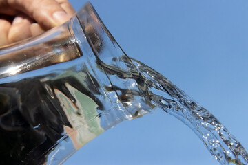 A Clear water flowing from a glass jug on a blue background.