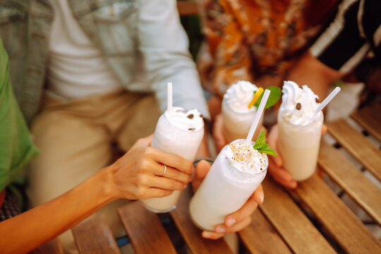 Iced milkshake. Young friends drinking milkshakes in a cafe. Summer refreshing drinks. Friendly lunch. - Powered by Adobe
