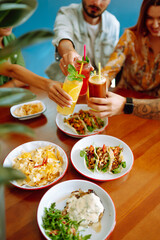 Happy friends having a great time in cafe. Young people sitting in a restorane having fun together, laughing, drinking cocktails and eating. Friendly dinner.