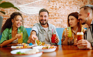 Happy friends having a great time in cafe. Young people sitting in a restorane having fun together, laughing, drinking cocktails and eating. Friendly dinner.