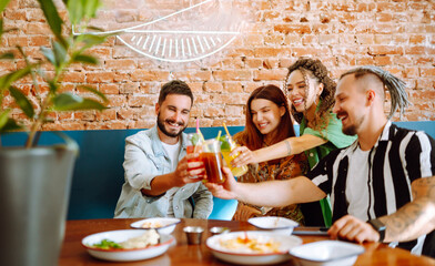 Happy friends having a great time in cafe. Young people sitting in a restorane having fun together, laughing, drinking cocktails and eating. Friendly dinner.