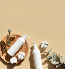 Beauty SPA branding mock-up. Natural organic eco cosmetics. White cosmetic bottles, cotton flowers, eucalyptus leaves with sun shadows on beige background flat lay top view. Blank label for branding