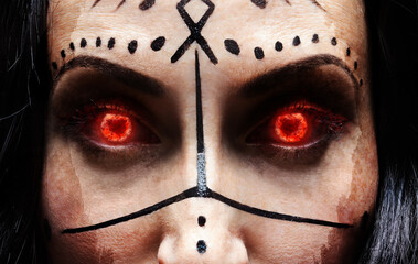 Сlose up face of mysterious woman (sorceress or witch) with fiery eyes and runic makeup. Halloween...