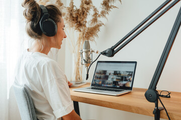 Female podcaster recording her podcast using microphone and laptop at his small home broadcast...