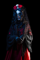Mysterious woman with Santa Muerte makeup in shawl and crown with skull and roses on black background. Halloween concept.