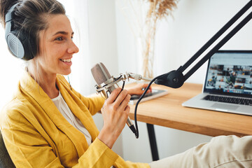 Female podcaster recording her podcast using microphone and laptop at his small home broadcast...