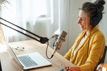 Woman working at home and talking into a microphone and recording podcast. Female working at...