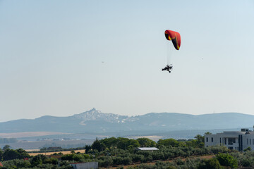 Side view of a powered Parachute. Ultralight Paramotor vehicle flying in the sky with green and mountains behind