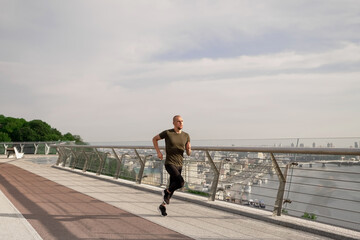 Young European man runs on the pedestrian bridge in the city at dawn. Healthy lifestyle concept. High quality photo