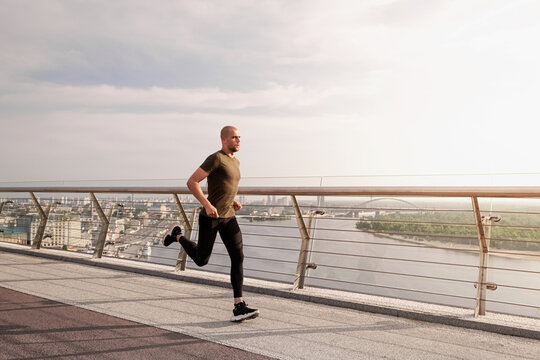 Young European man runs on the pedestrian bridge in the city at dawn. Healthy lifestyle concept. High quality photo