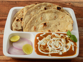 Indian combo meal Paneer Butter Masala with Naan, served over a rustic wooden background, selective focus