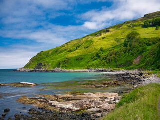 Obraz premium The clear blue water and green hills around Murlough Bay on the spectacular Antrim Causeway Coast in Northern Ireland, UK - taken on a calm, sunny day in summer with blue sky and blue water.