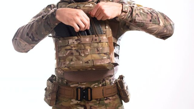 Special operations officer in multicam camouflage inserts loaded rifle magazines into pouches at plate carrier with white background