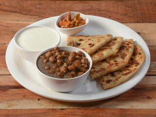 Aloo Paratha or Indian Potato stuffed Flatbread and channa masala Served with fresh curd and pickle. isolated over a rustic wooden background, selective focus