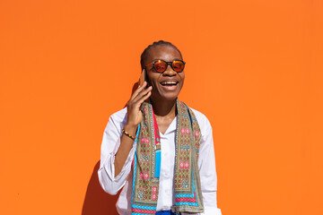 Chica africana empresaria con expresión de felicidad, hablando por teléfono, en fondo naranja con...