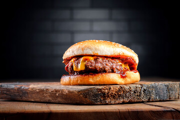 A classic small cheeseburger with barbecue sauce on a wooden board against a black brick wall. BBQ...