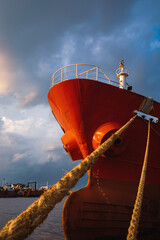 Low angle view of cargo ship docked at port against rain cloudy sky at sunset time in vertical frame