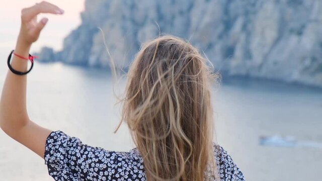 beautiful girl enjoying the breeze by the sea at a height at sunset. The girl gracefully moves enjoying the sunset in the mountains by the sea feeling the breeze and breathing the fresh sea air