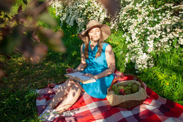 A young lady with a book in her hands on a picnic in the park squints from the sun
