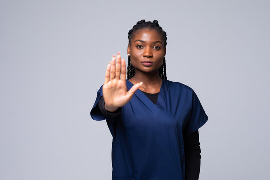 Young beautiful African American doctor woman doing stop gesture with palm of the hand. Warning expression with negative and serious gesture on the face over gray background.