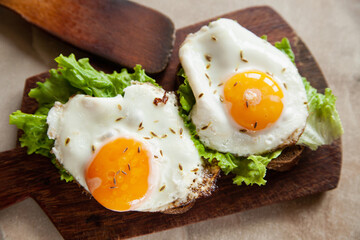 Closeup yummy toasts with fried eggs and lettuce leaves for breakfast placed on wooden board
