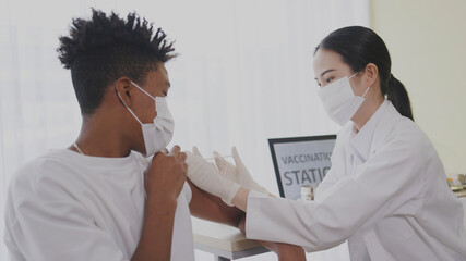Obraz premium African American teenager wearing face mask sit in hospital waiting for COVID-19 vaccination. Epidemic Control with Inject at Clinic. Concept health care