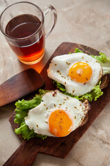 Delicious toasts with fried eggs and lettuce leaves for breakfast placed on table near cup of hot tea in morning