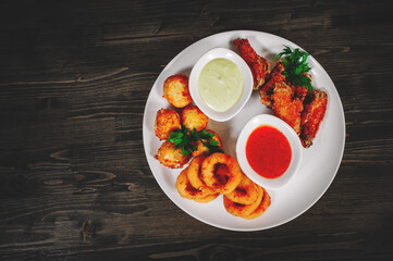 snacks to beer. cheese balls, chicken wings, onion rings, sauce on a wooden background. with copy space. top view