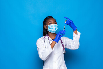 Syringe in hand of african american doctor in medical mask on blurred background isolated on blue