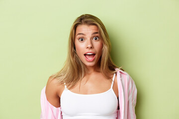 Close-up of attractive blond woman in pink shirt, looking surprised, open mouth fascinated,...