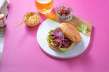 Pastrami burger with mustard, beer and pickels over bright pink background