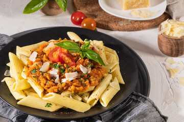 Tasty appetizing classic italian penne pasta with vegetarian lentil bolognese sauce, cheese parmesan and basil on plate on light table. Healthy eating concept.