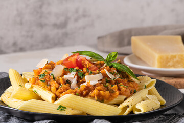 Tasty appetizing classic italian penne pasta with vegetarian lentil bolognese sauce, cheese parmesan and basil on plate on light table. Healthy eating concept.