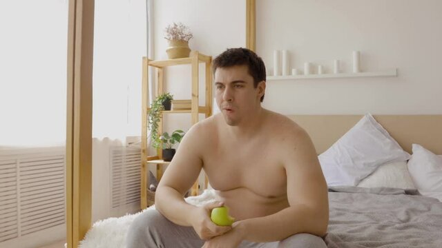 Fat guy sticks to a diet and eats an apple to lose weight. Man sits at home in quarantine during a pandemic covid 19.