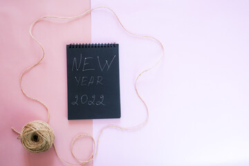 Fototapeta na wymiar New Year's composition. Black notebook cover and New Year's inscription on a pink background. Flat lay, top view, copy space 